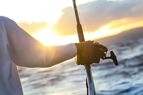 Man Holding A Fishing Rod watching the sunset over the water