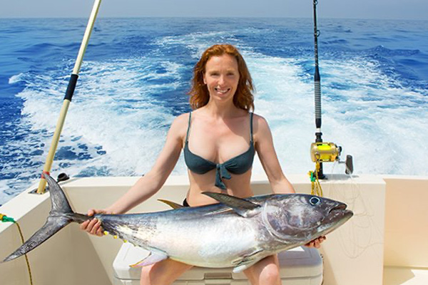 Woman sitting in the back of a charter fishing boat holding a large fish